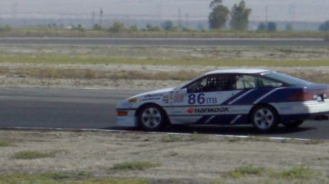 1990 Ford Probe - A white race car with blue accents and the number 86 is seen on a racetrack.