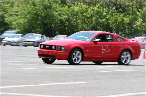 2001 Mercury Grand Marquis - A red Ford Mustang with racing number 65 participates in an autocross event, with other vehicles blurred in the background.