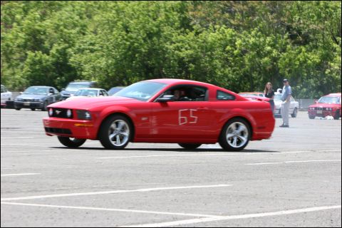 2001 Mercury Grand Marquis - A red Ford Mustang with racing number 65 is seen on a paved lot during an event.
