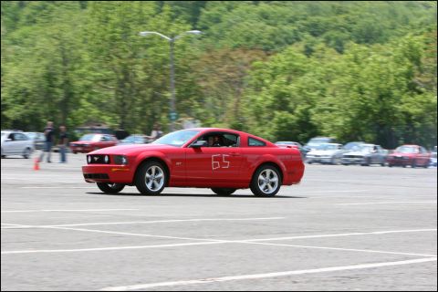 2001 Mercury Grand Marquis - A red Ford Mustang with racing number 65 participates in an event on a paved lot.