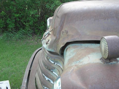 1951 Chevrolet C/K Pickup - Close-up of a heavily rusted truck's front end, showing a distinctive grille and damaged hood.