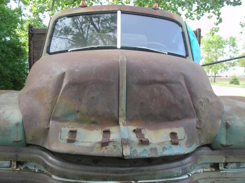 1951 Chevrolet C/K Pickup - Front view of a heavily rusted truck, showing a dented hood and split windshield.