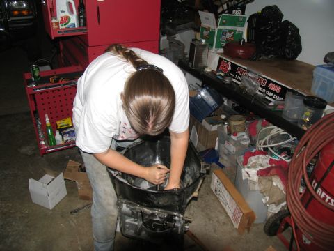 1978 Ford Bronco - A person is shown working on a vehicle transmission in a garage setting with various tools and parts around.