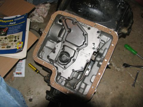 1978 Ford Bronco - Close-up of an automatic transmission pan with a new gasket, ready for reassembly. Tools and a repair manual are visible.