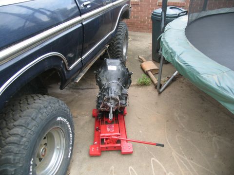 1978 Ford Bronco - A dark blue 1978 Ford Bronco is parked outdoors with a transmission removed and placed on a red jack.