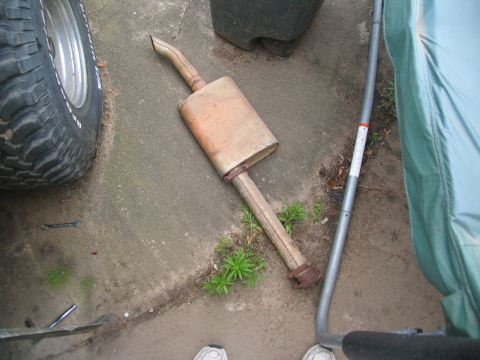 1978 Ford Bronco - Exhaust muffler and pipe on the ground, with a tire and green cover nearby.