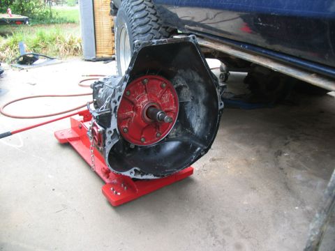 1978 Ford Bronco - A vehicle's transmission is removed and placed on a red jack, with the vehicle's tire and undercarriage visible above.