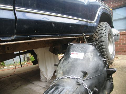1978 Ford Bronco - Transmission removed from a dark blue vehicle, revealing rust on the frame and a white cloth covering part of the undercarriage.