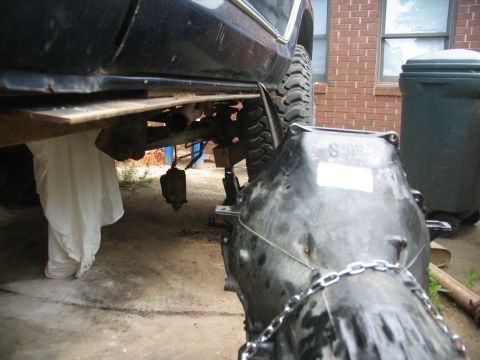 1978 Ford Bronco - Transmission and undercarriage of a vehicle being worked on, with a large black transmission unit in the foreground.