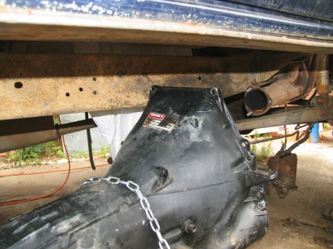 1978 Ford Bronco - A transmission component is visible beneath a vehicle's frame, with a chain secured to it.