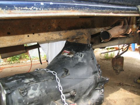 1978 Ford Bronco - Close-up view of a vehicle's transmission assembly, showing a chain and a label attached to the casing.