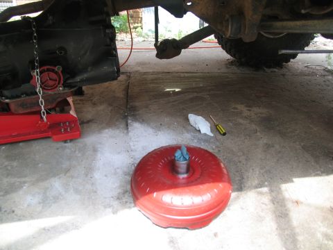 1978 Ford Bronco - A red torque converter and a transmission are visible, along with a screwdriver and rag on the ground.