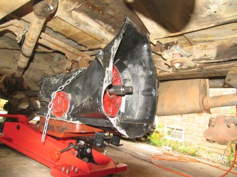 1978 Ford Bronco - A vehicle's transmission is being lowered for service, revealing undercarriage components.