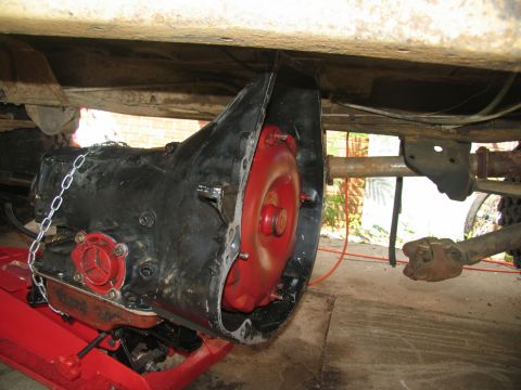 1978 Ford Bronco - Transmission and torque converter assembly being worked on, supported by a red jack under a vehicle.