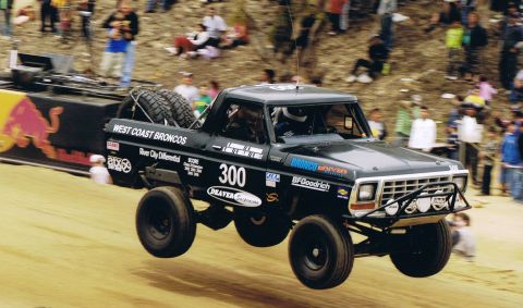 1990 Ford Bronco - black West Coast Broncos Ford race truck number 300 launches off a jump in front of a packed grandstand crowd.