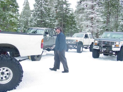 1986 Ford Bronco - Several modified trucks are parked in a snow-covered wooded area.