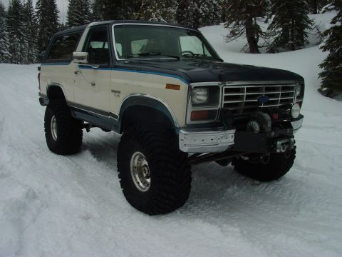 1986 Ford Bronco - A lifted, two-tone Ford Bronco with a winch sits in a snowy landscape, its large tires ready for off-road conditions.