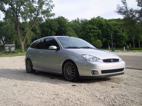 2003 Ford Focus - A silver 2003 Ford Focus is parked on a gravel lot with trees and a sign in the background.