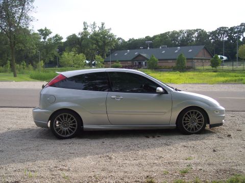 2003 Ford Focus - A silver 3-door hatchback is parked on a gravel lot with a building in the background.