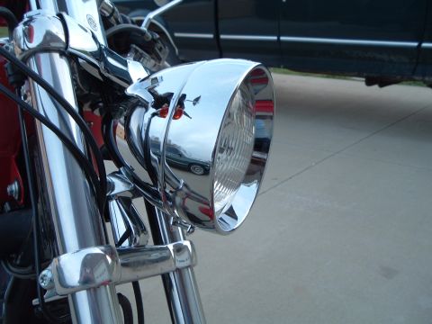 2002 Harley-Davidson Sportster Custom - Close-up of a motorcycle's chrome headlight assembly, with a dark SUV reflected in its surface.