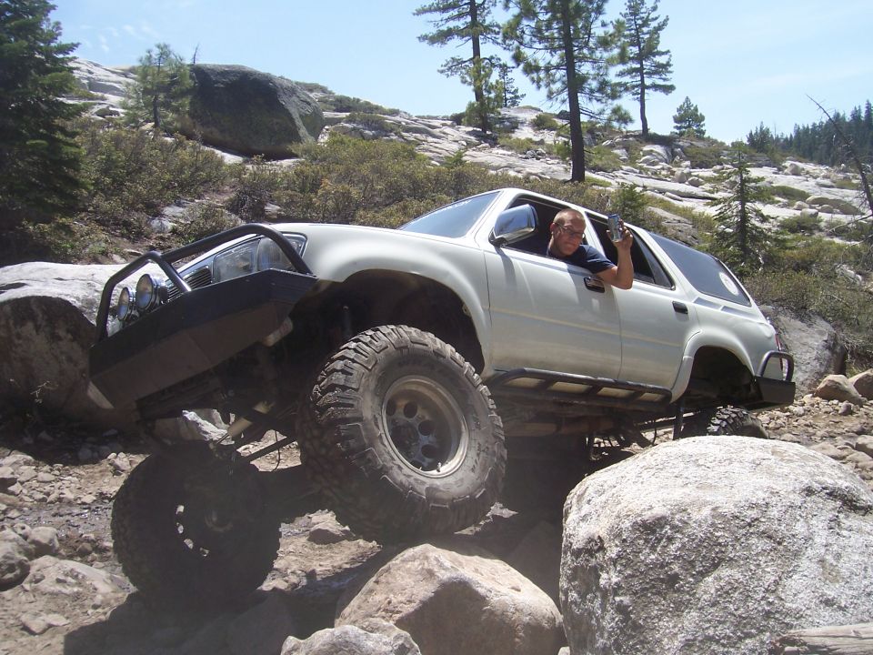 White lifted SUV rock crawling over granite boulders with driver leaning out the window