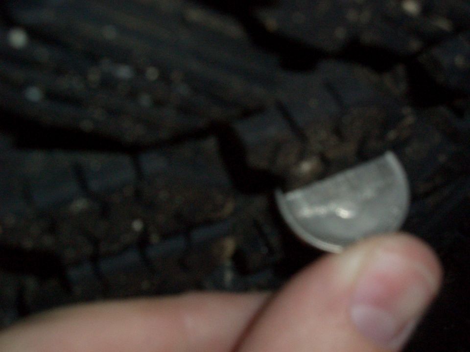 Hand inserting a quarter into tire tread grooves to check tread depth