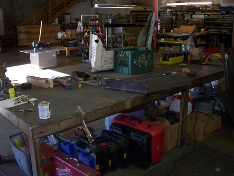 1991 Ford Bronco - A cluttered workshop scene with various tools and vehicle components laid out on a large workbench.