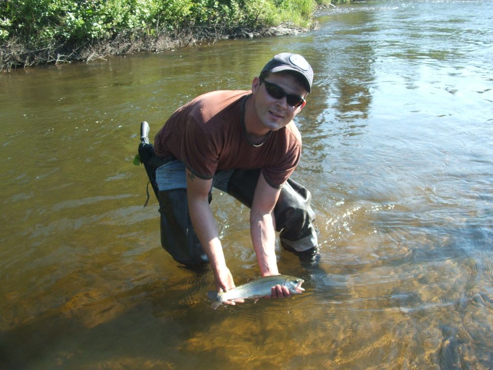 Man in waders holding a trout in a river