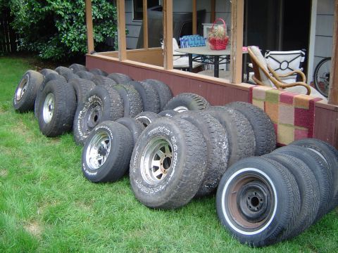 1989 Ford Bronco - A collection of tires and wheels are stored on the lawn next to a house's porch.