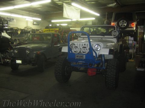 1987 Suzuki Samurai - Two Jeeps are parked inside a garage, with a third vehicle elevated in the background.