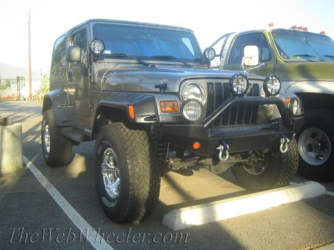 1987 Suzuki Samurai - A gray Jeep Wrangler is parked in a lot, with a large green truck beside it.