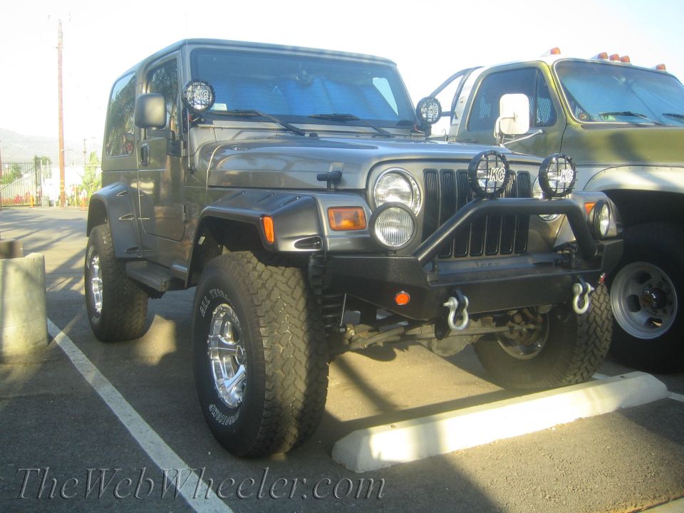 Gray Jeep Wrangler with aftermarket bumper and lights parked next to a green truck
