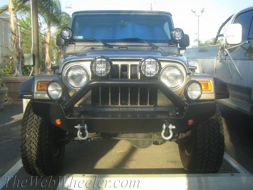 Tan Jeep Wrangler front view with KC lights and bull bar. Jeep logo visible