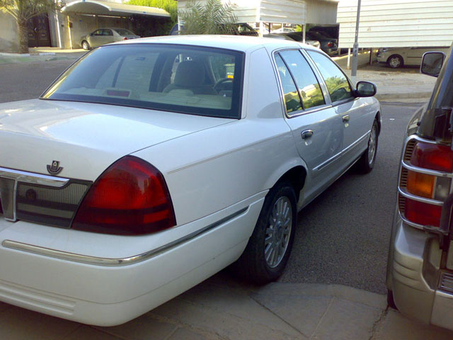 White Mercury Grand Marquis sedan, rear three-quarter, parked by a carport
