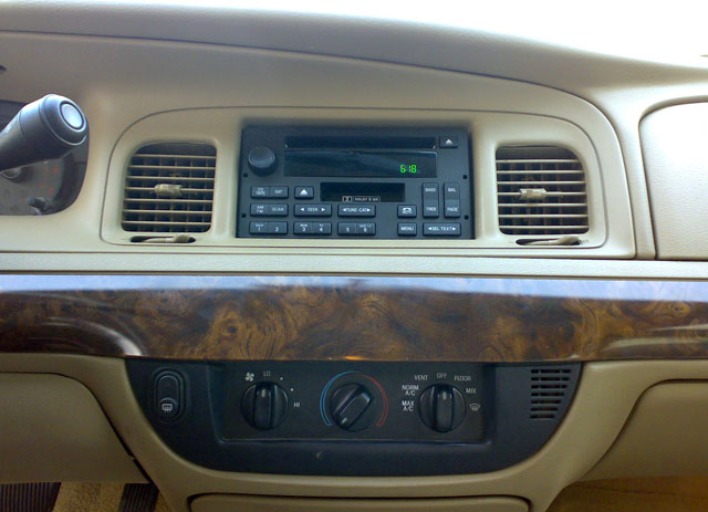 Car dashboard with radio, vents, and climate controls. Wood trim accents the dash