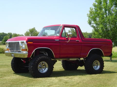 1978 Ford Bronco - Lifted 1978 Ford Bronco with large tires sits on a grassy field under a clear blue sky.