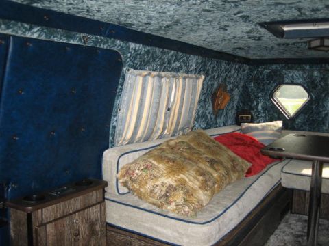 1978 Ford E250 - Custom interior of a van conversion shows a bed, seating area, and a unique diamond-shaped window.