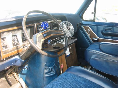 1978 Ford E250 - The interior of a vintage Ford van features blue upholstery, wood-grain trim, and a dashboard with gauges.
