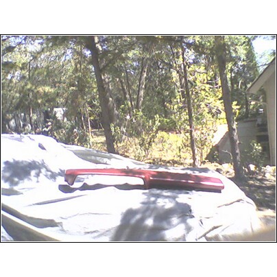 1973 Ford Ranchero - A red trim piece, possibly for a vehicle, rests on a tarp in an outdoor setting with trees in the background.