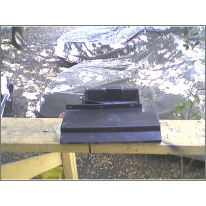 1973 Ford Ranchero - A black plastic car part is displayed on a wooden workbench outdoors.