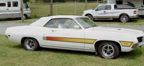 1976 Ford Ranchero - A white convertible muscle car is parked on grass with a pickup truck and RV in the background.