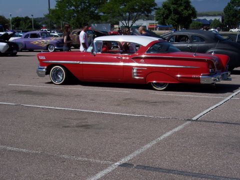 1972 Ford Ranchero - A red and white 1958 coupe with chrome accents and whitewall tires is parked in a lot with other vehicles.