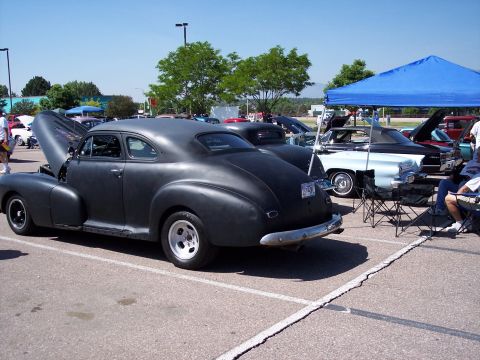 1972 Ford Ranchero - Several cars are parked at an outdoor event, with one matte black coupe prominently displayed with its hood up.