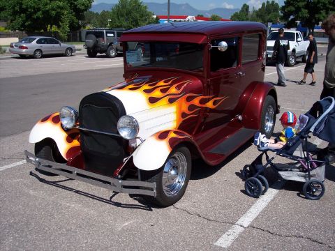 1972 Ford Ranchero - A custom hot rod with flame decals is parked in a lot, with a child in a stroller nearby.