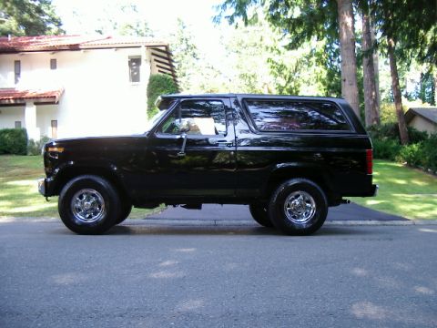 1986 Ford Bronco - This black SUV, likely from the 1980s, is viewed from the side with chrome wheels and tinted windows.