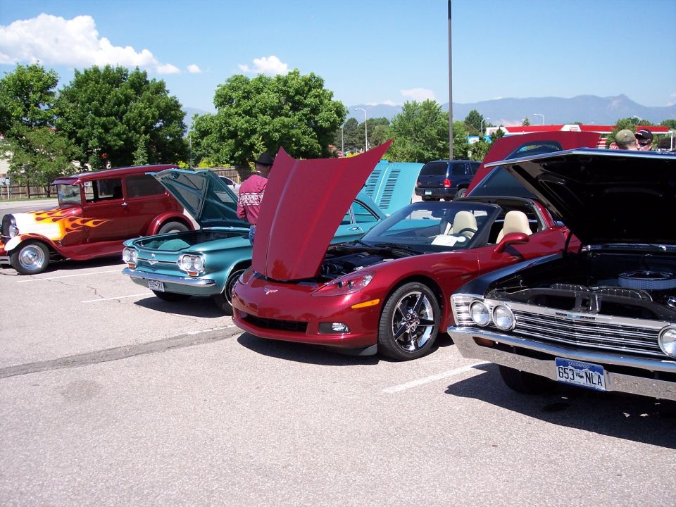 Several cars parked in a lot, some with hoods open. Includes a red convertible, a teal coupe, and a red sedan with flames