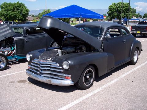 1972 Ford Ranchero - Matte black 1947 Chevrolet coupe on display with hood open, another custom car behind it.