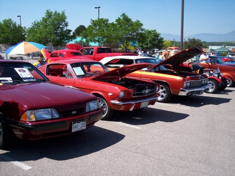 1972 Ford Ranchero - Several classic cars are parked in a lot, with their hoods open, under a bright blue sky.