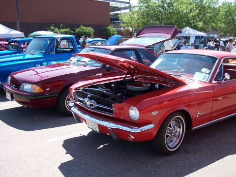 1972 Ford Ranchero - Multiple vehicles are on display at an outdoor event, with one red classic car's hood open.