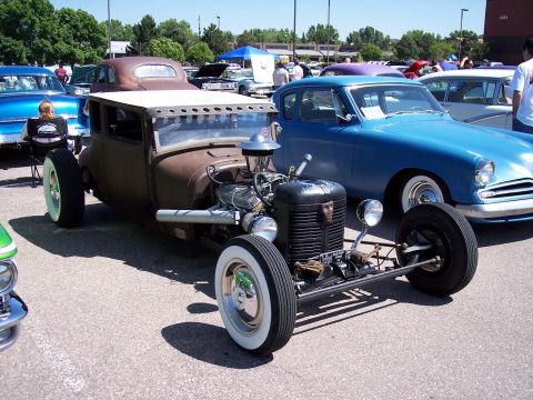1972 Ford Ranchero - A custom-built rat rod is displayed at an outdoor car show with other vehicles in the background.